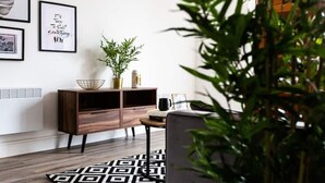 A modern living room with a wooden cabinet, a black and white patterned rug, and a potted plant. - Staycay - Modern 1-bed Apartment in Manchester City Centre (Salford)