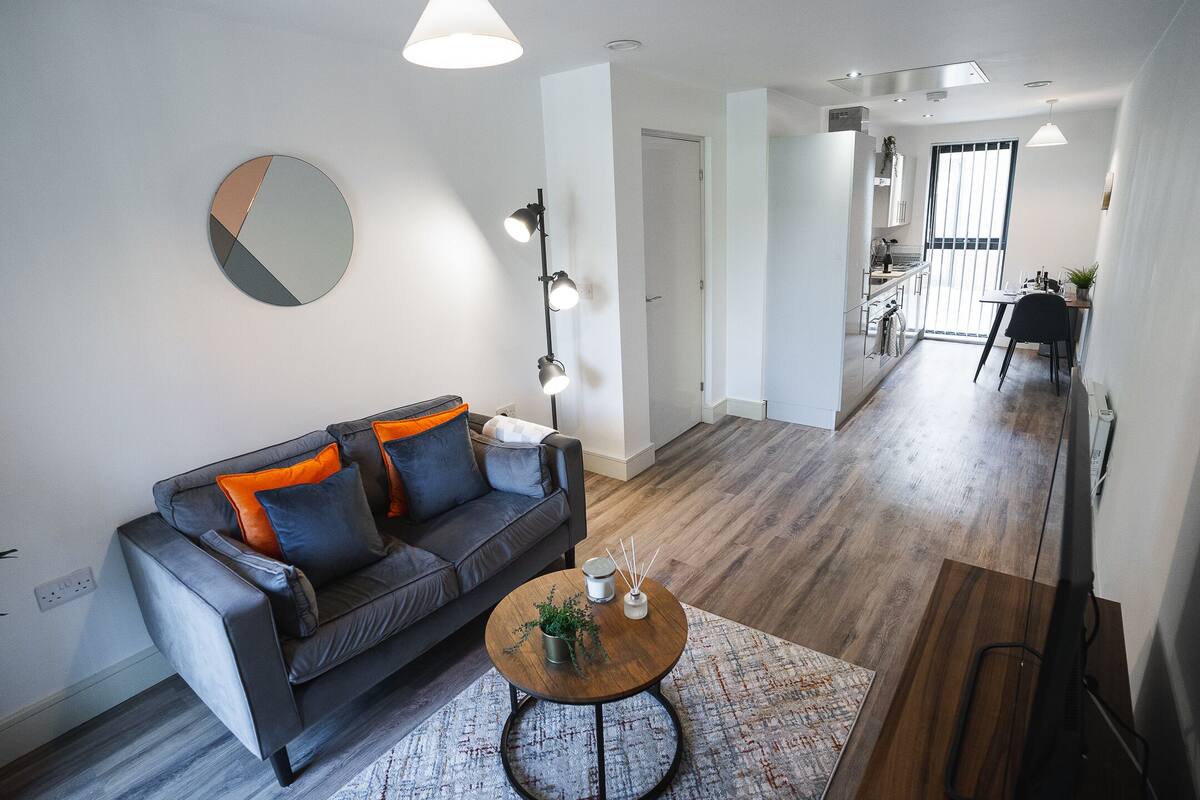 A modern living room with a grey sofa, a round coffee table, and a large mirror on the wall.