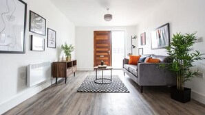 A modern living room with a grey sofa, a wooden cabinet, a black and white rug, and a large plant. - Staycay - Modern 1-bed Apartment in Manchester City Centre (Salford)