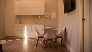 Une cuisine moderne avec des meubles blancs, une table à manger avec deux chaises et un téléviseur à écran plat fixé au mur.