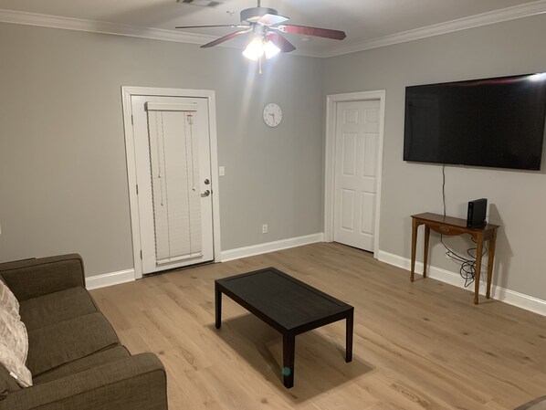 Una sala de estar con ventilador de techo, televisor de pantalla plana montado en la pared y una mesa de centro de madera.