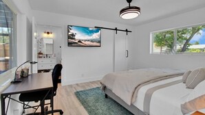 Un dormitorio moderno con cama, escritorio, silla y un ventanal grande.
