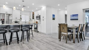 Una cocina moderna con armarios blancos, una isla central con taburetes y una zona de comedor con sillas de madera.