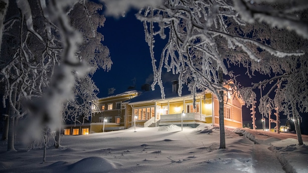 Et snedækket landskab med en bygning, der har en veranda og mange vinduer.