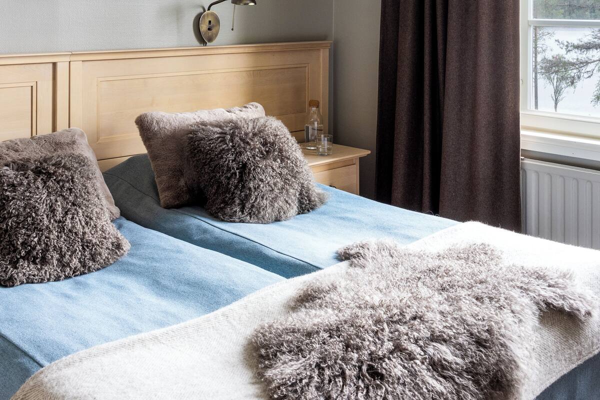Una camera da letto con un letto, due cuscini soffici, un comodino con una lampada, un quadro appeso al muro e una finestra con tende.