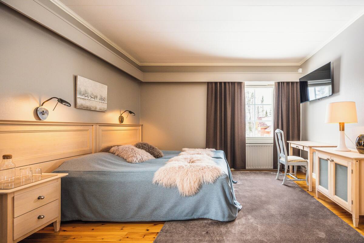 Una camera da letto con un letto, comodini, una scrivania, una sedia, una TV e una finestra con tende.