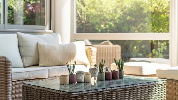 Un salón acogedor con una mesa de centro de mimbre, un sofá blanco y varias plantas en macetas.