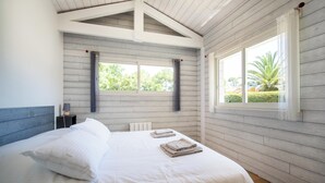 Un dormitorio con una cama grande, dos ventanas con cortinas, una mesita de noche con lámpara y vistas al exterior.