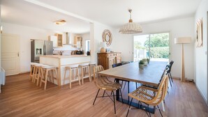 Una cocina amplia con una isla central, taburetes de madera y una gran mesa de comedor con sillas de mimbre.