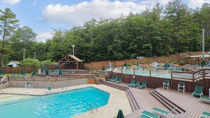 Uma área de piscina com deck de madeira, espreguiçadeiras e um espaço de estar coberto.