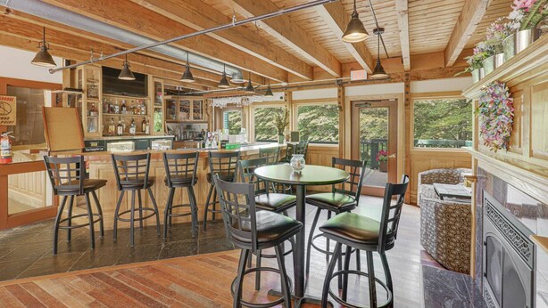 Um interior rústico com vigas de madeira, um espaço de bar e uma área de jantar com cadeiras e uma mesa.