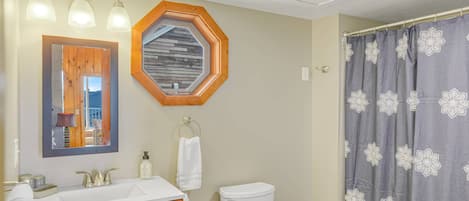A bathroom with a wooden vanity, a white toilet, a shower curtain with a floral pattern, and a hexagonal mirror with a wooden frame.