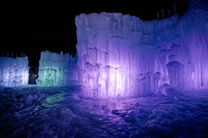 A nighttime ice sculpture with illuminated sections in purple and green.