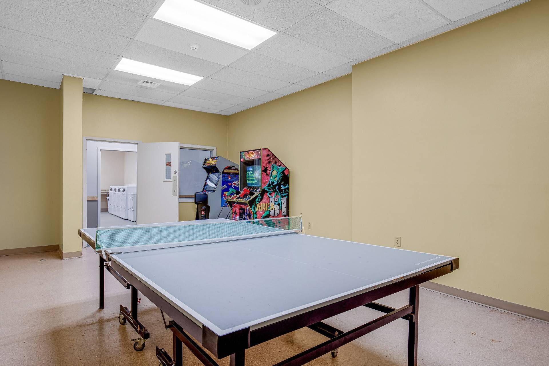 A room with a ping pong table, a vending machine, and a door leading to a laundry area.