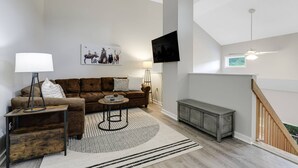 A modern living room with a brown sofa, a coffee table, a floor lamp, a TV mounted on the wall, and a staircase leading to an upper level. - Lidos Lodge (Lincoln)