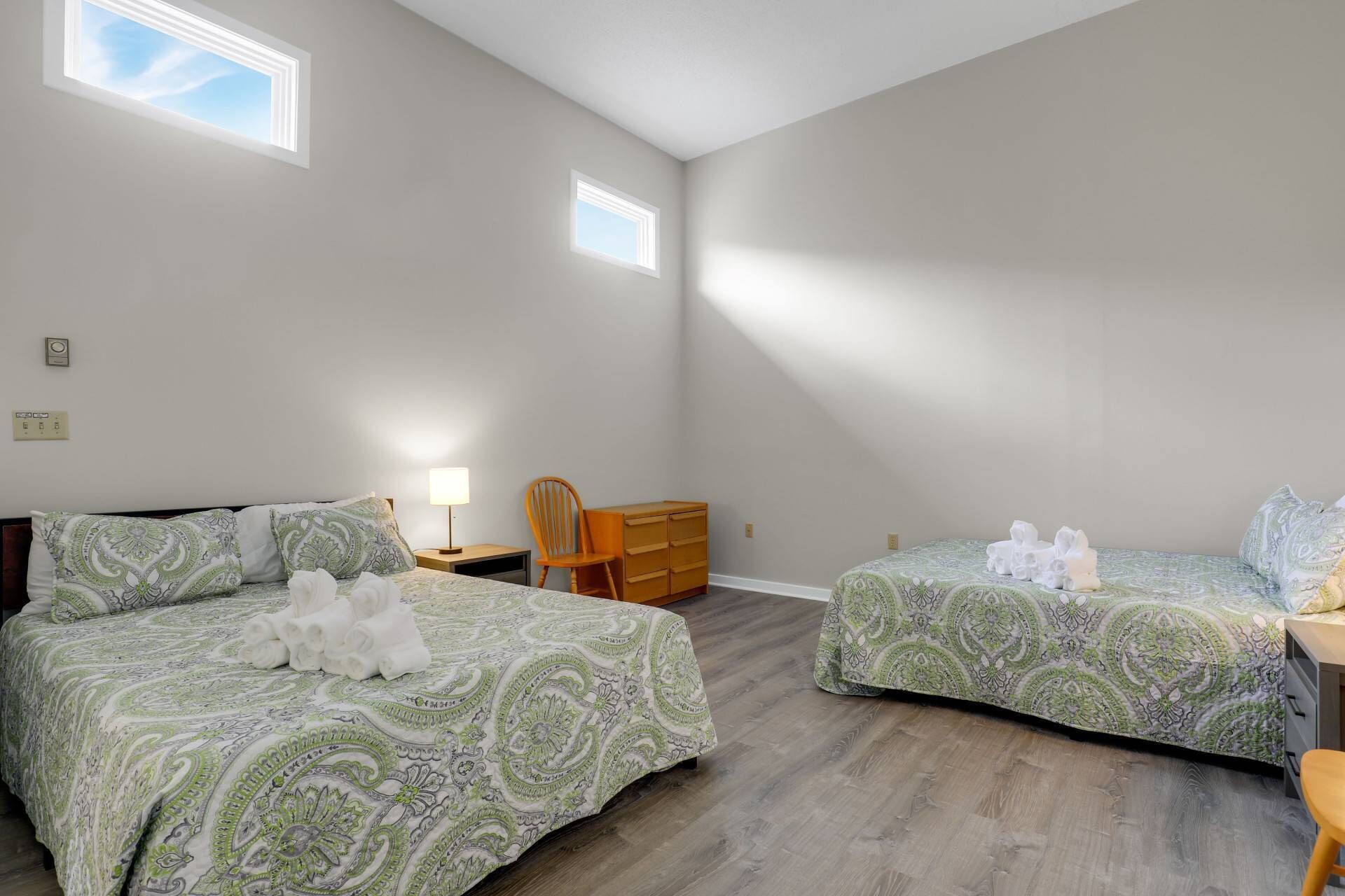 A bedroom with two beds, a chair, a dresser, and a lamp.