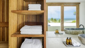 A wooden shelf with white towels, a stone bathtub, and a view of the ocean.