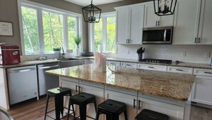 Een keuken met een groot eiland, witte kasten, een magnetron en barstoelen.