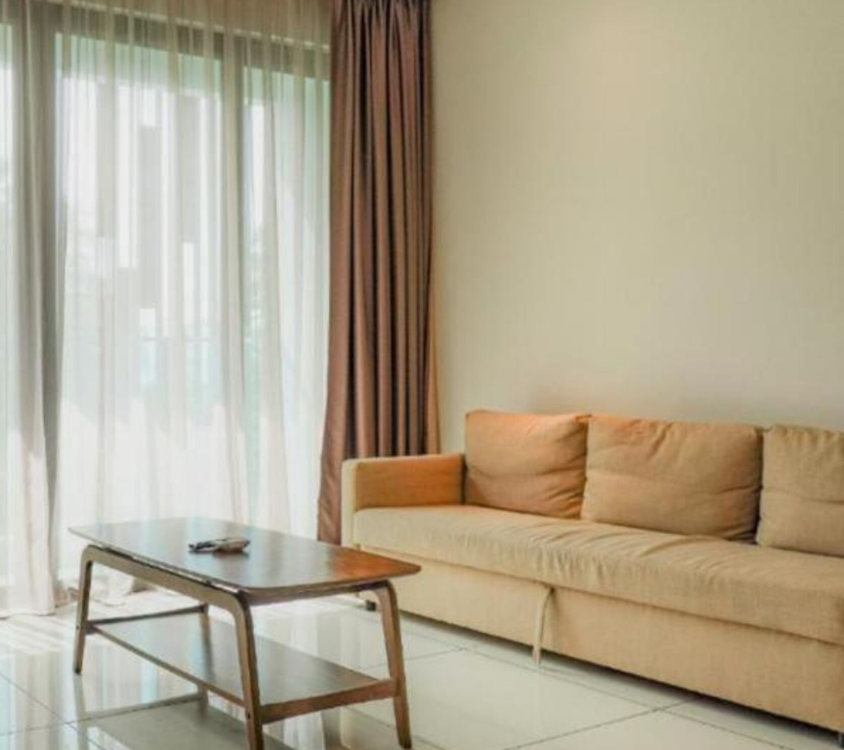 Una sala de estar con una mesa de vidrio, un sofá color crema y cortinas translúcidas.