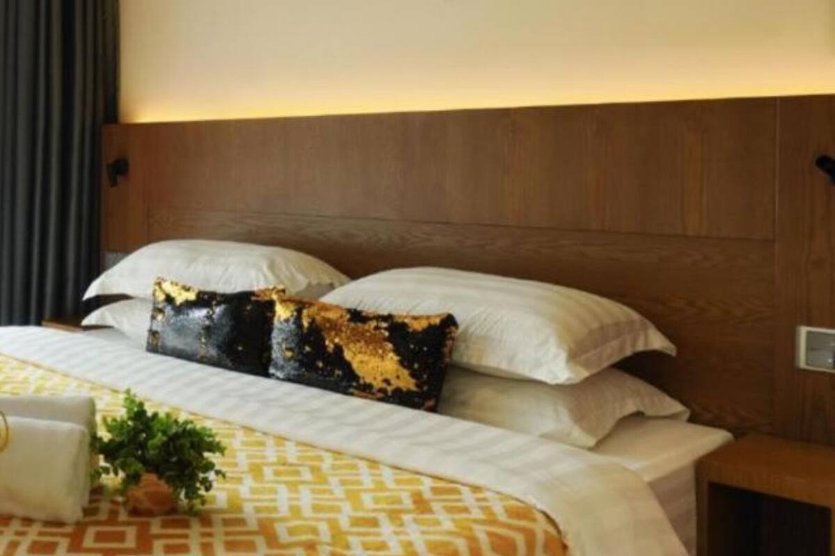Une chambre d’hôtel avec une tête de lit en bois, un lit recouvert d’une literie blanche à motifs et un seul coussin décoratif.