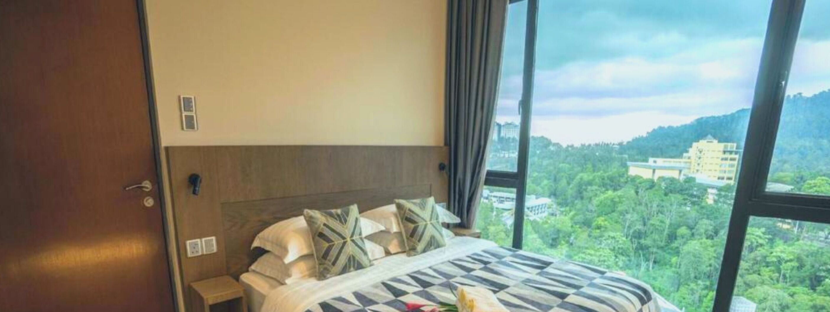 Habitación de hotel con un ventanal grande, cama con ropa de cama estampada y vistas a un paisaje verde.