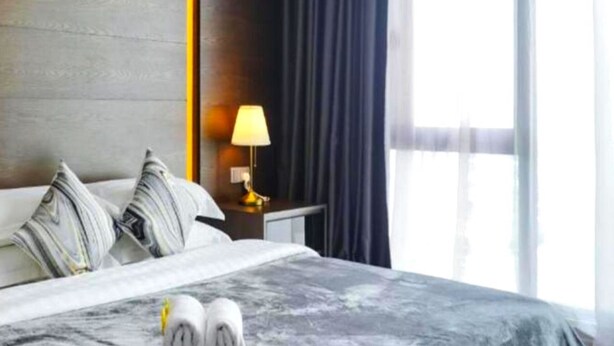A hotel room with a bed, pillows, a nightstand with a lamp, and a window with curtains.