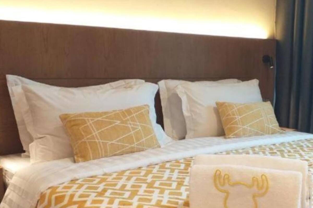 Une chambre d’hôtel avec une tête de lit en bois, deux oreillers blancs, une couvre-lit à motifs et une fenêtre avec des rideaux.