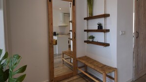 Un couloir avec une porte coulissante donnant sur un espace cuisine. On y trouve des étagères en bois ornées de plantes et un banc en osier.