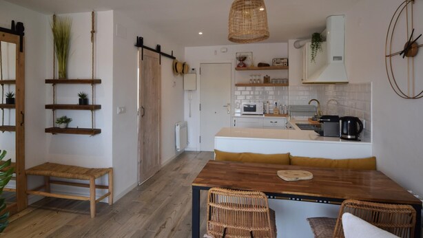 Une cuisine moderne avec une table à manger en bois, des chaises en osier et un luminaire suspendu.