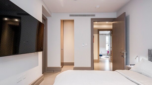 A modern hotel room with a large bed, a flat-screen TV mounted on the wall, and a bathroom visible through an open door.