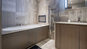 A modern bathroom with a large bathtub, a glass-enclosed shower, and a wooden vanity with a mirror.