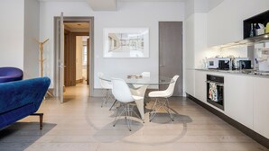A modern kitchen with white cabinets, a built-in oven, and a dining area with a glass table and white chairs.