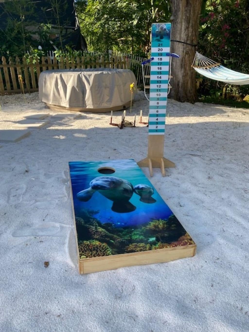 A board game setup with a numbered board, a hammock, and a tent in a sandy outdoor area.