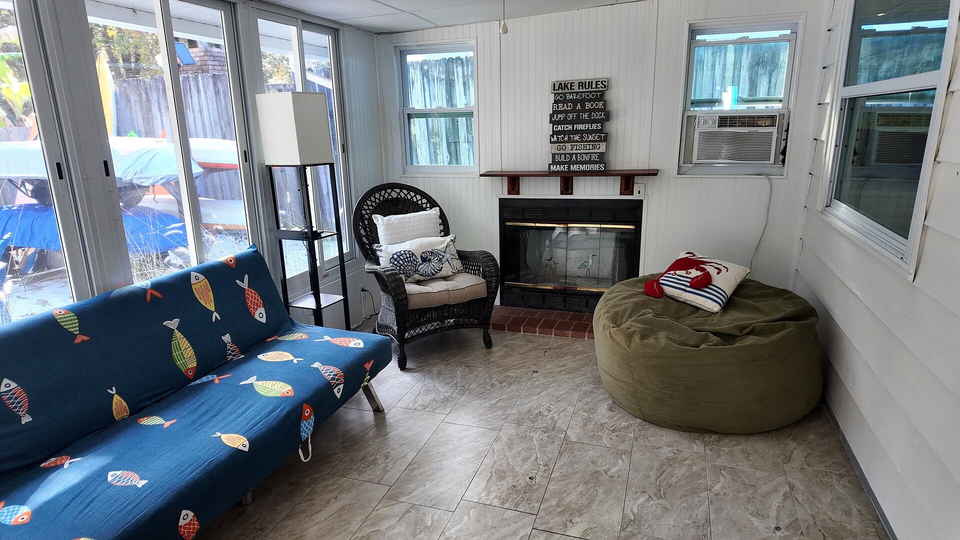 Une pièce chaleureuse avec un canapé bleu, un fauteuil en osier, un pouf vert, une cheminée et un panneau indiquant les règles à respecter au bord du lac.
