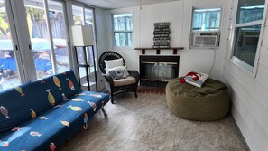 A cozy room with a blue sofa, a wicker chair, a green bean bag, a fireplace, and a sign with lake rules. - River Beach Retreat: Tiki Bar, Hot Tub, Kayaks&BBQ (Spring Hill)