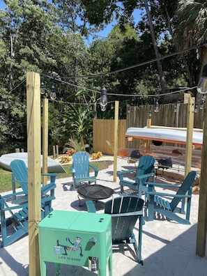 An outdoor patio area with blue Adirondack chairs, a small round table, and a green utility box with a cartoon character. - River Beach Retreat: Tiki Bar, Hot Tub, Kayaks&BBQ (Spring Hill)