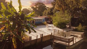 A dock with wooden benches, a small house, and a garden with banana plants. - River Beach Retreat: with Tiki Bar, Fire Pit, Hot Tub & Clear Kayak (Spring Hill)