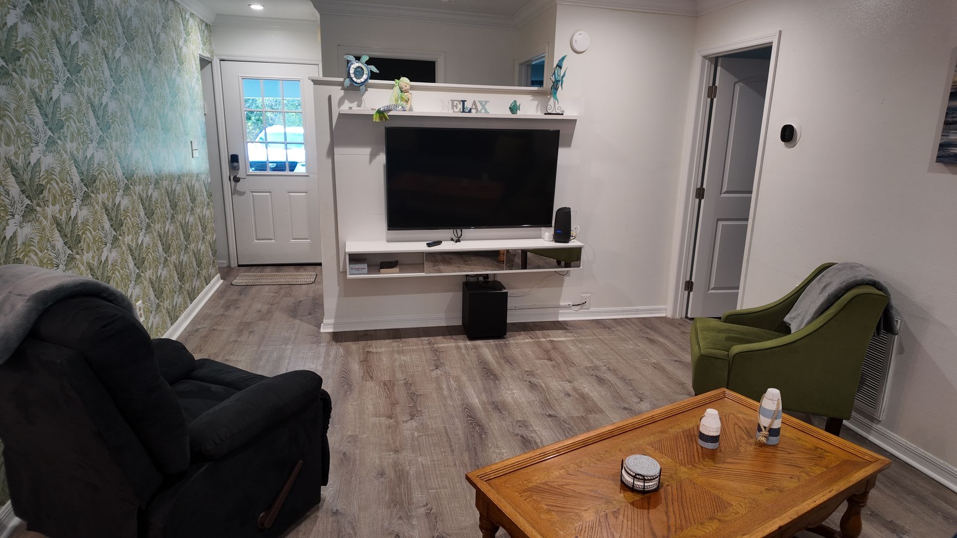 A living room with a TV on a white stand, a green armchair, a black sofa, and a wooden coffee table.