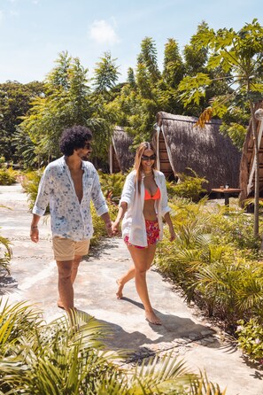 A pathway surrounded by lush greenery and a thatched-roof structure. - AMALIFE Beach Club & Hotel (Cartagena)