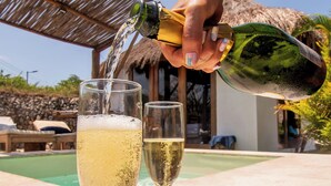 A hand pouring a drink into a glass, with a pool and a thatched roof structure in the background. - AMALIFE Beach Club & Hotel  (Cartagena)