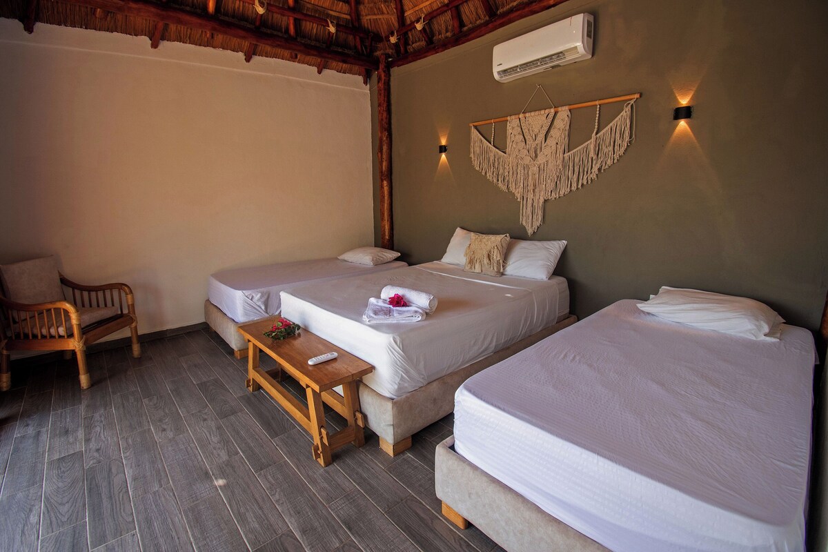 A room with two beds, a wooden table, a chair, and a wall-mounted air conditioner.