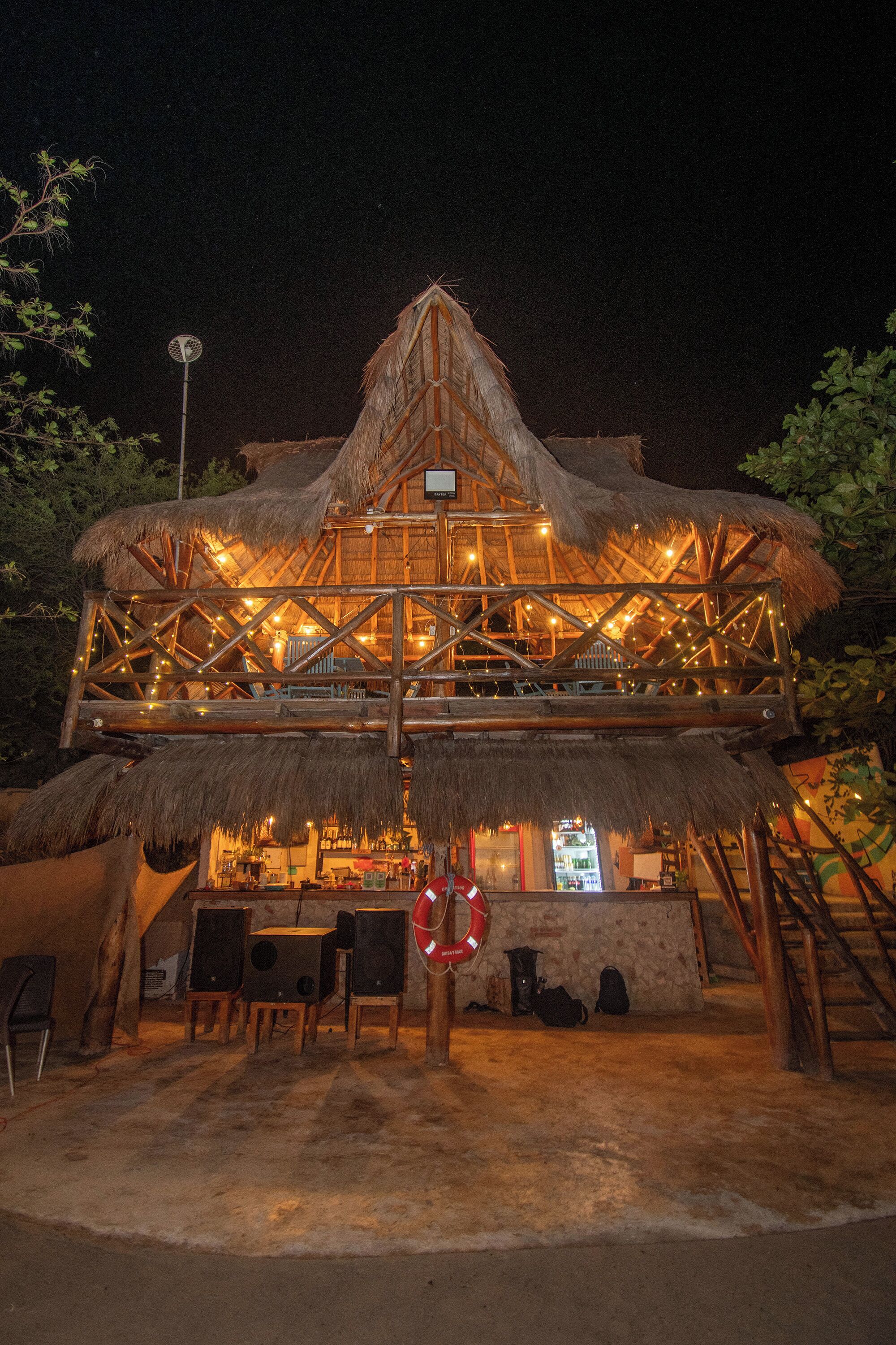 A thatched-roof structure with a wooden deck and seating area, surrounded by trees.