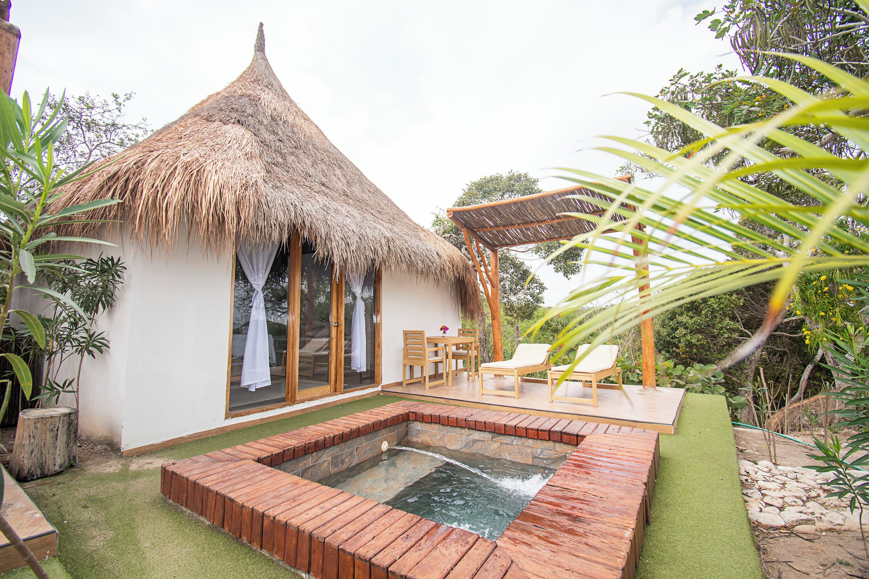 Ein Haus mit einem Reetdach, einem Schwimmbad, einer Holzterrasse und Gartenmöbeln.