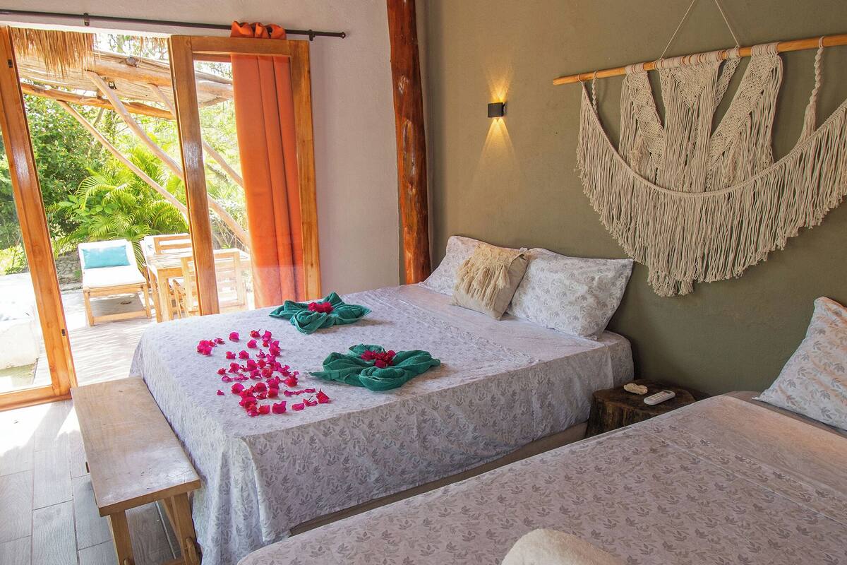 A room with two beds, an air conditioner, a macrame wall hanging, and a bench.