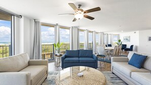Un ampio soggiorno con una grande finestra, un ventilatore a soffitto e vista sull'oceano.