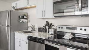 A modern kitchen with stainless steel appliances, white cabinetry, and granite countertops. - Sandcastle Condominium Unit 102 (Port Aransas)