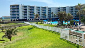 A hotel with multiple balconies, a swimming pool, and a fenced lawn area. - Sandcastle Condominiums Unit 107 (Port Aransas)