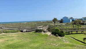 A coastal property with a wooden deck, a pathway leading to a blue house, and a view of the ocean. - Sandcastle Condominiums Unit 107 (Port Aransas)