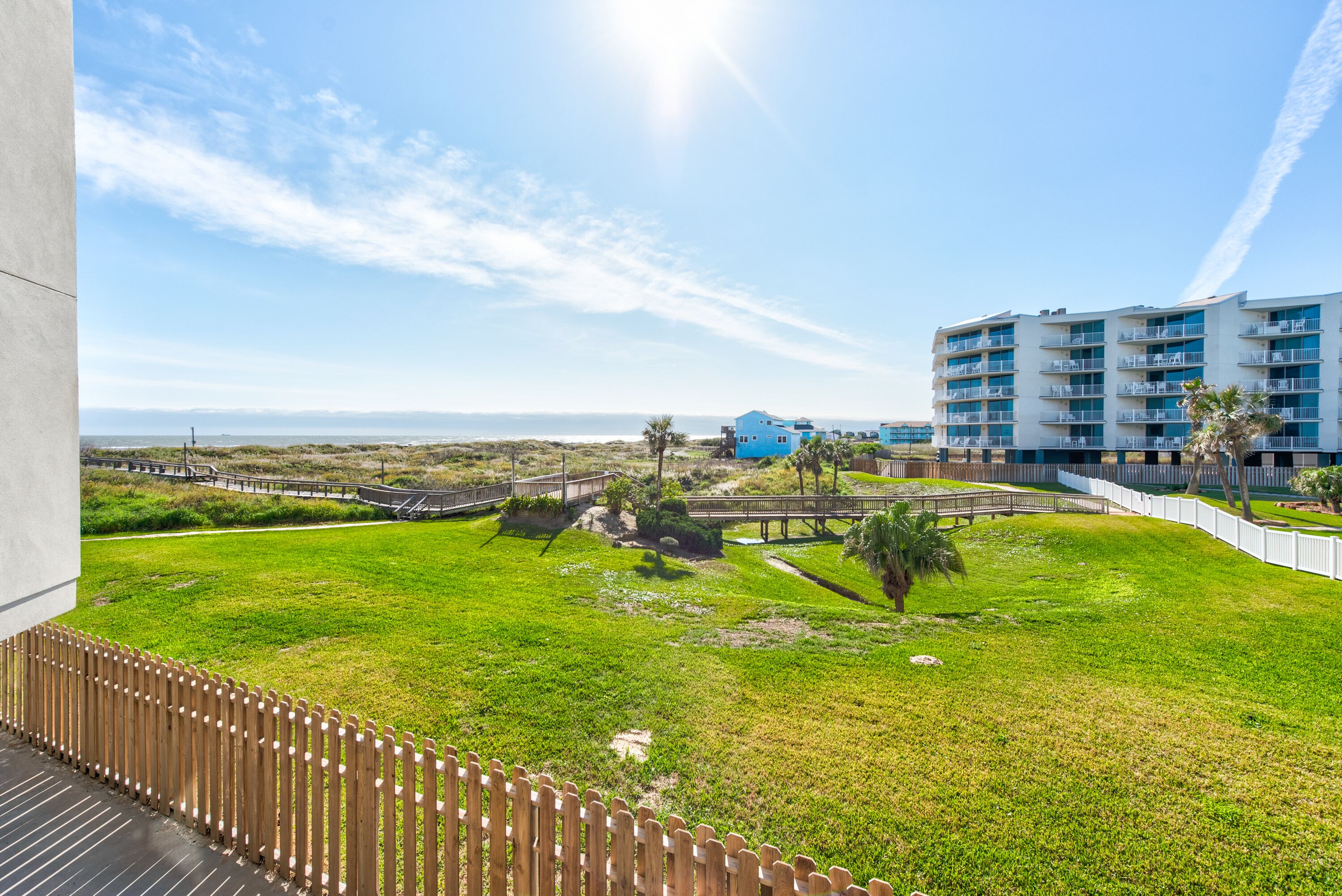 A hotel with a view of the beach, a wooden deck, and a fenced garden area.
