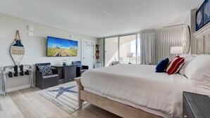 A modern hotel room with a large bed, a flat-screen TV, a balcony with curtains, and a view of the cityscape. - Sandcastle Condominiums Unit 107 (Port Aransas)